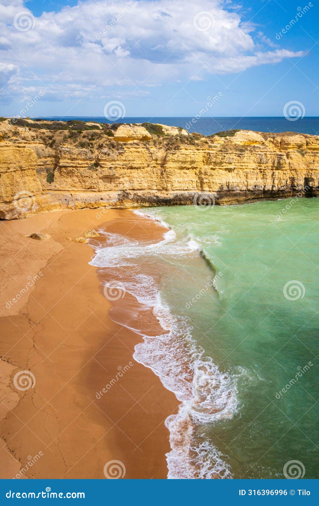 vertical view of cliffs and ocean waves crashing onto beach near albufeira, portugal
