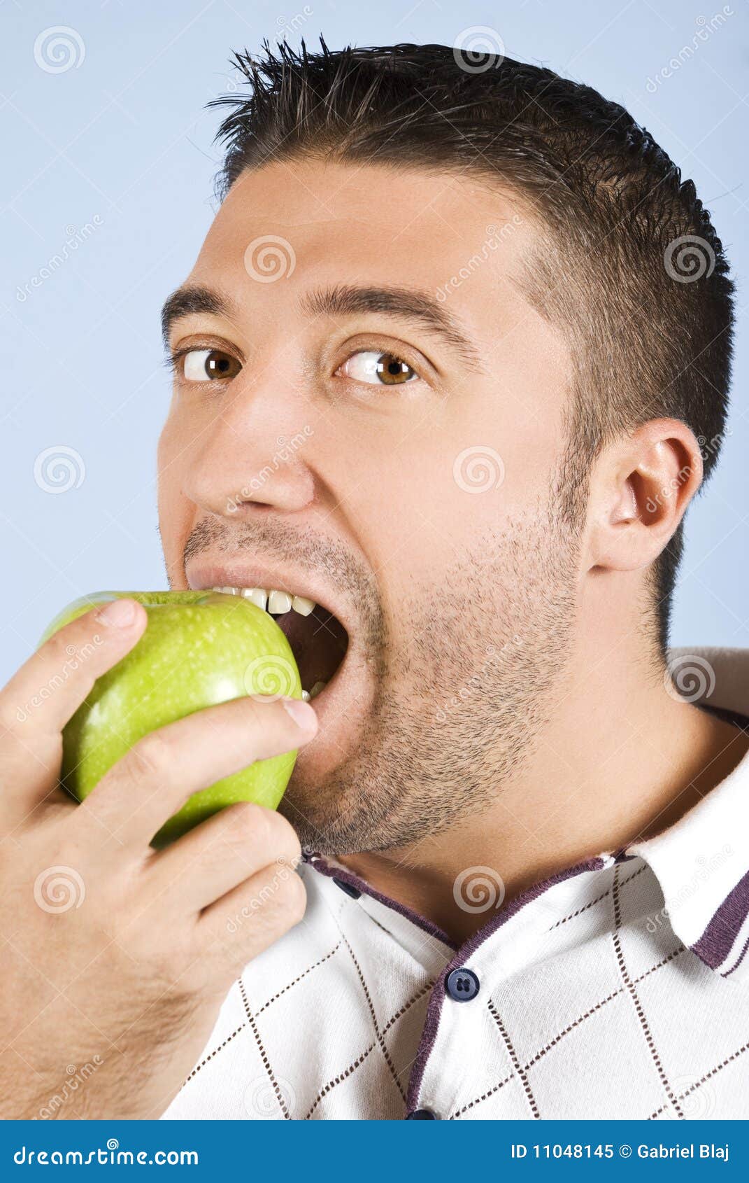 La verticale mâle prenant un dégagement d'une pomme et vous regardant sur le fond bleu, contrôlent également mes <a href="http://www.dreamstime.com/healthy-life-people-rcollection11192-resi828293">gens en bonne santé de durée de</a> ramassage