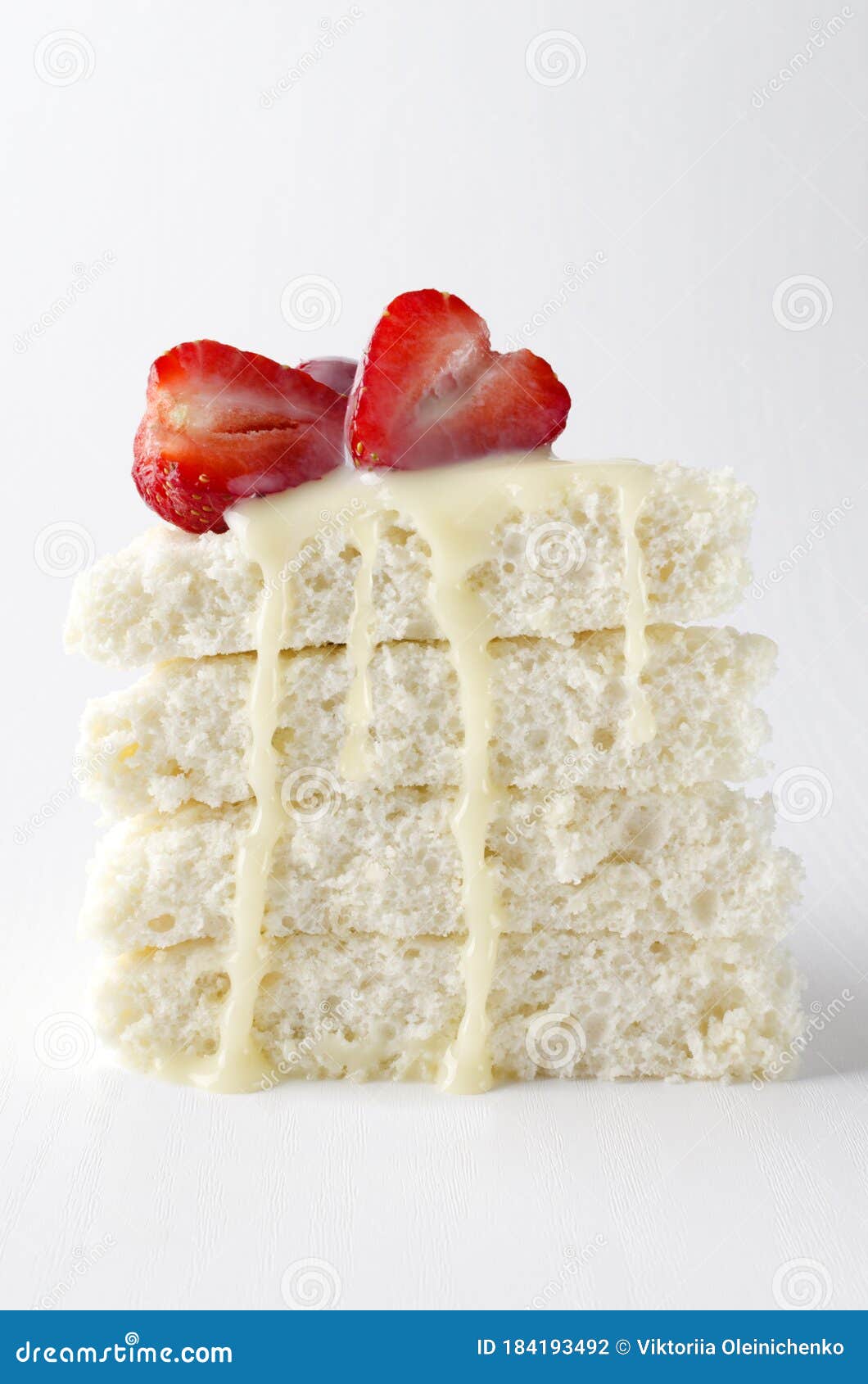 verticl image.piece of biscuit cake with slices of strawberry and condensed milk on the white background