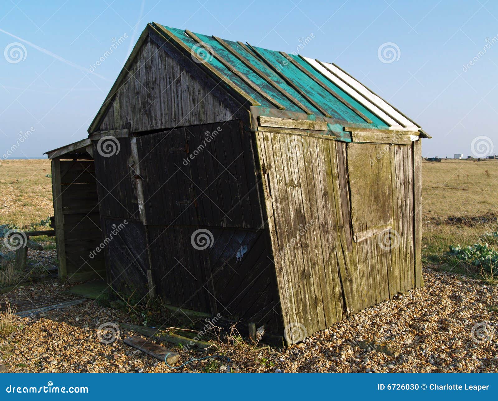 Vertiente vieja. El viejo decaimiento verde vertió en la playa abandonada de Dungeness, Kent. Reino Unido. Con las sombras del bastidor del sol de la última tarde.