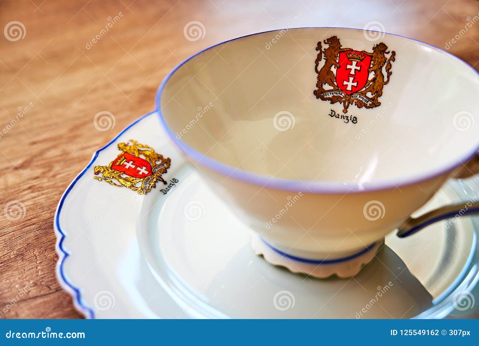 very old vintage cup with a plate on a wooden table, both with `danzig` written on it underneath the city`s coat of arms