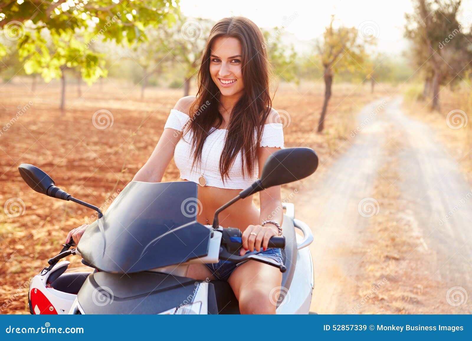 Vespa de motor del montar a caballo de la mujer joven a lo largo de la carretera nacional