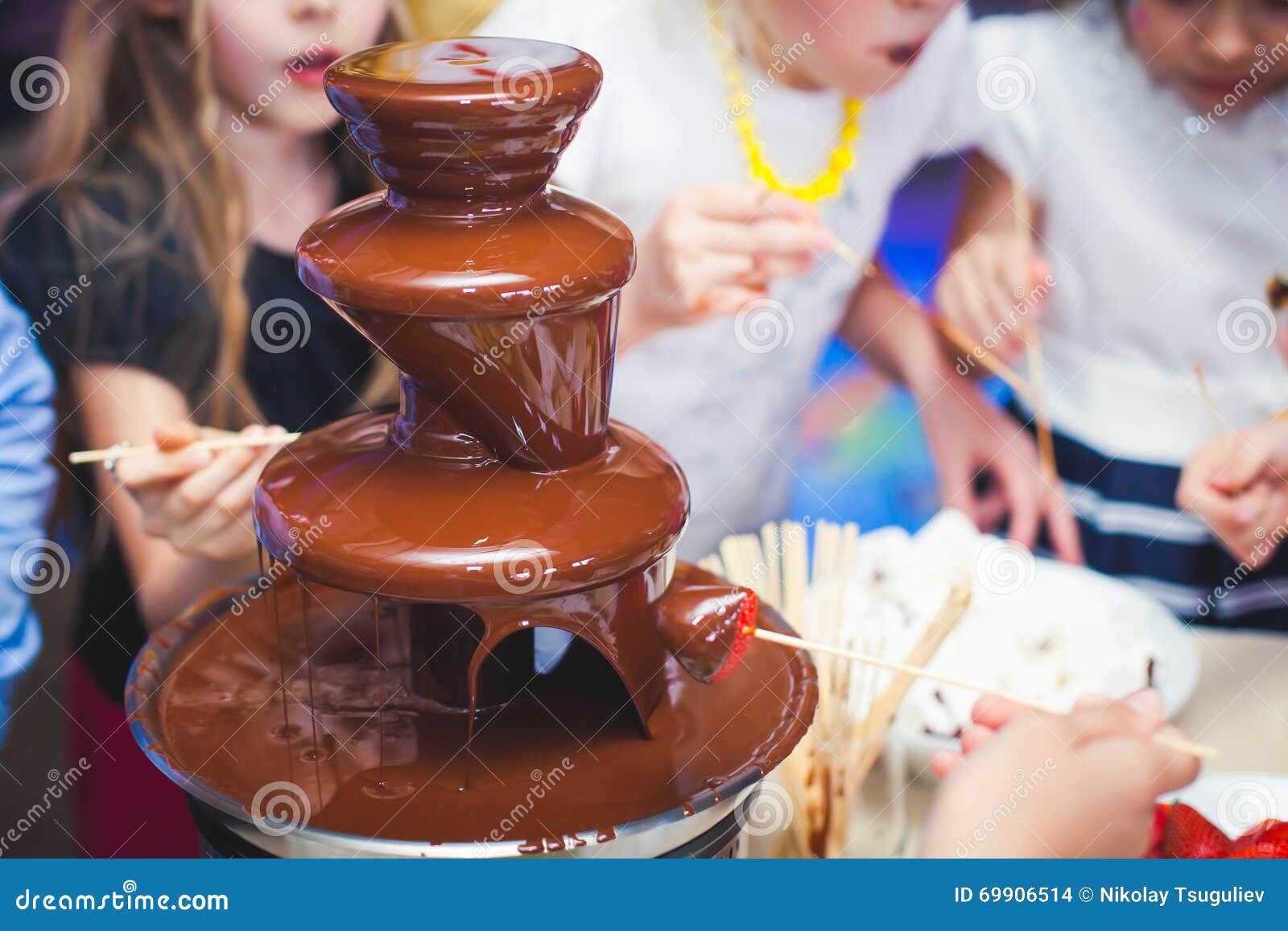 vibrant picture of chocolate fountain fontain on childen kids birthday party with a kids playing around and marshmallows and fruit