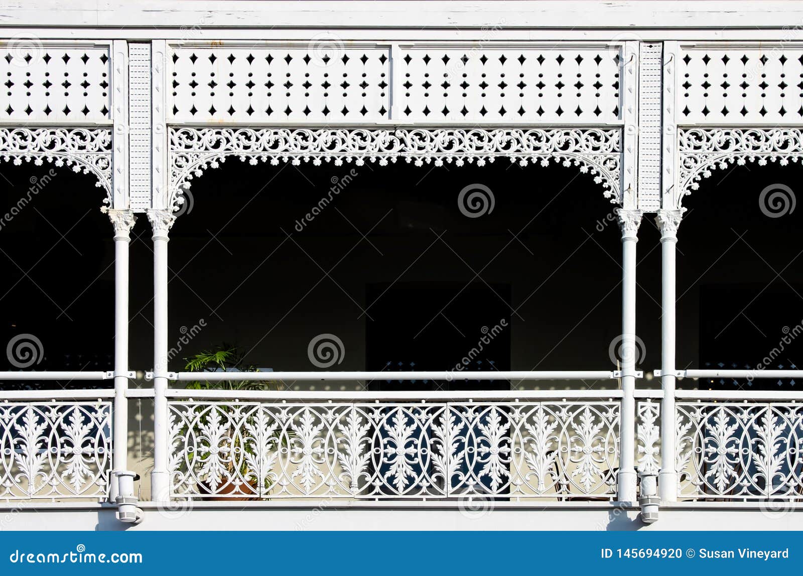 victorian decorative wrought iron balcony with a plant on it but mostly darkness behind the white painted ornate railings -