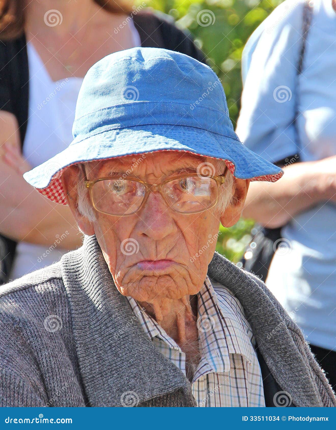 Foto de un viejo hombre gruñón que tira de una cara y que lleva un sombrero azul del verano.
ideal de la foto para los accesorios etc. de las expresiones faciales, del personas mayores, de vestir.