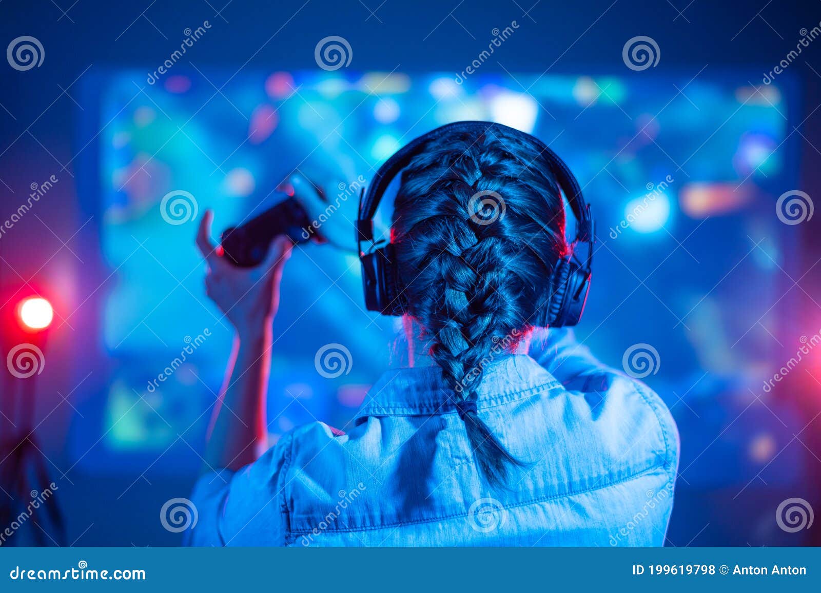 Girl in headphones plays a video game on the big TV screen. Gamer with a  joystick.