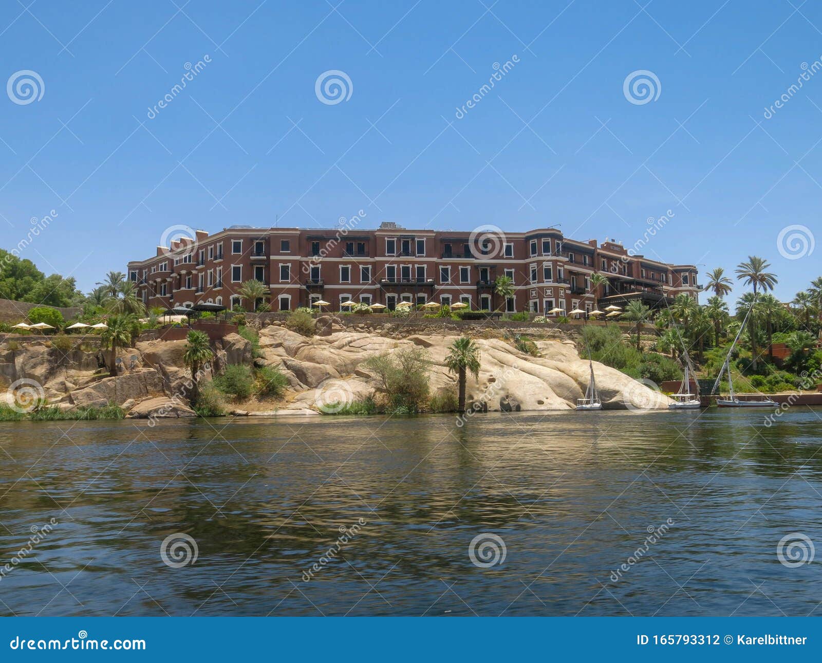a view from a boat on a three-story building with a brown facade on the shore of lake nasser in egypt. architecturally nice