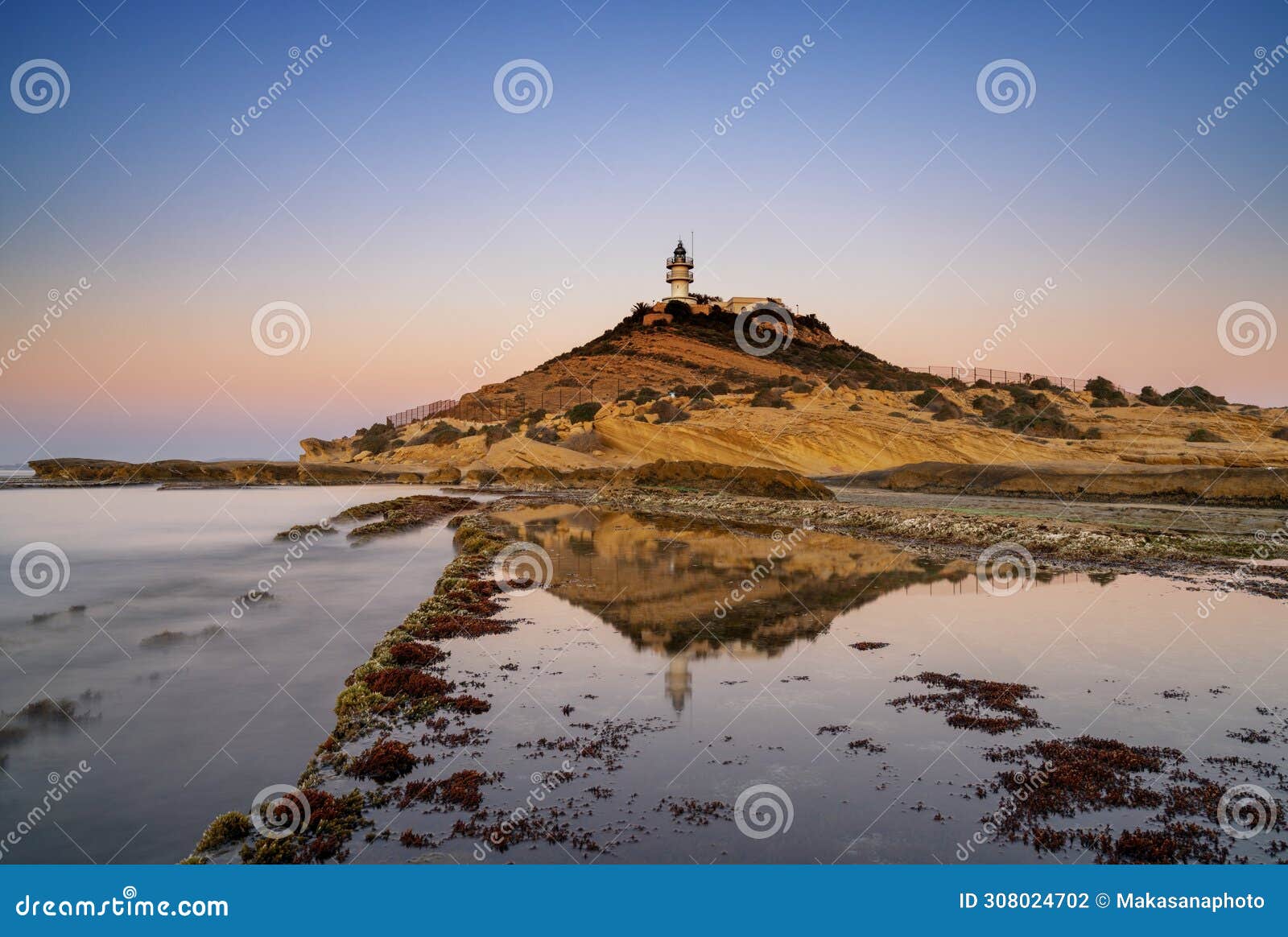 view of the cabo de la huerta lighthouse at sunrise with reflections in tidal pools in the foreground