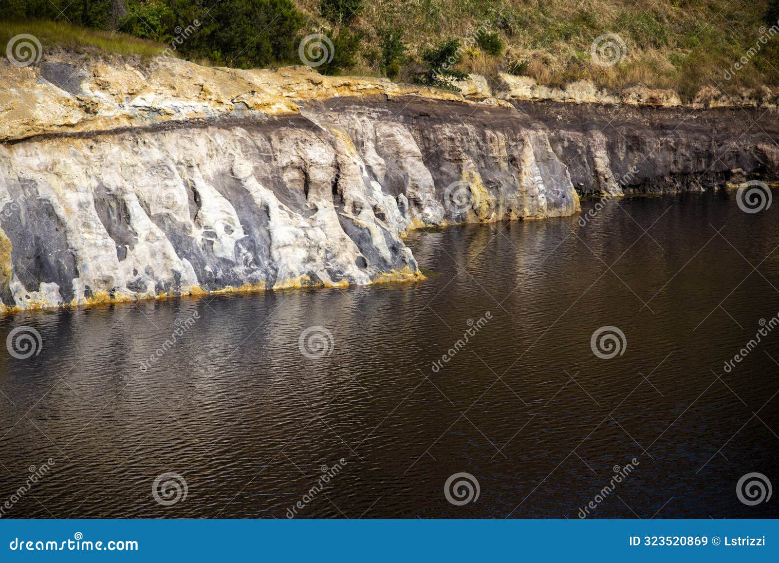 view of the jagged rock face with mineral residues at the edge of the lake, solfatara locality, pomezia, rome, italy