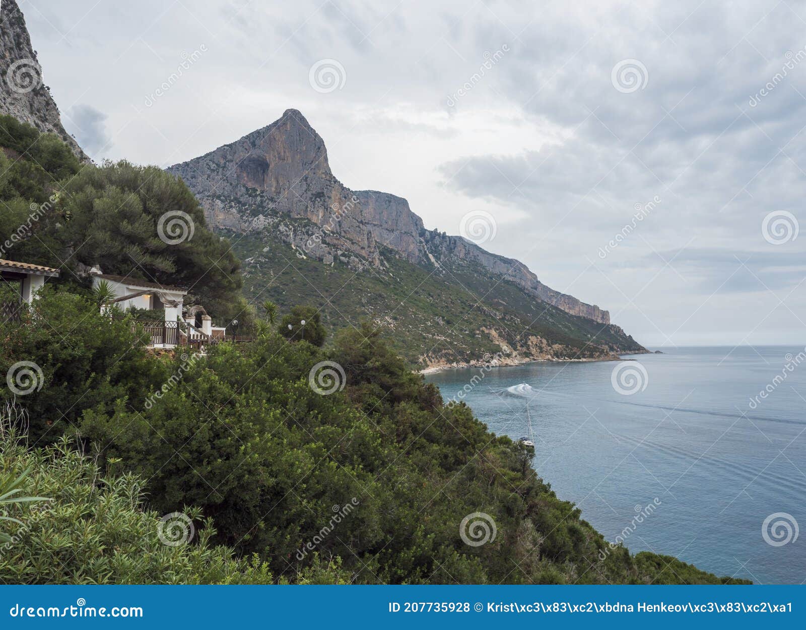 view over gulf of orosei from pedra longa with limestone cliffs, green bushes, restaurante house and turquoise blue