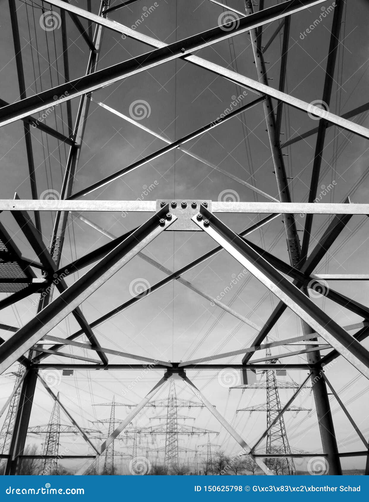view through steel struts on 3 rows of power poles in black and white