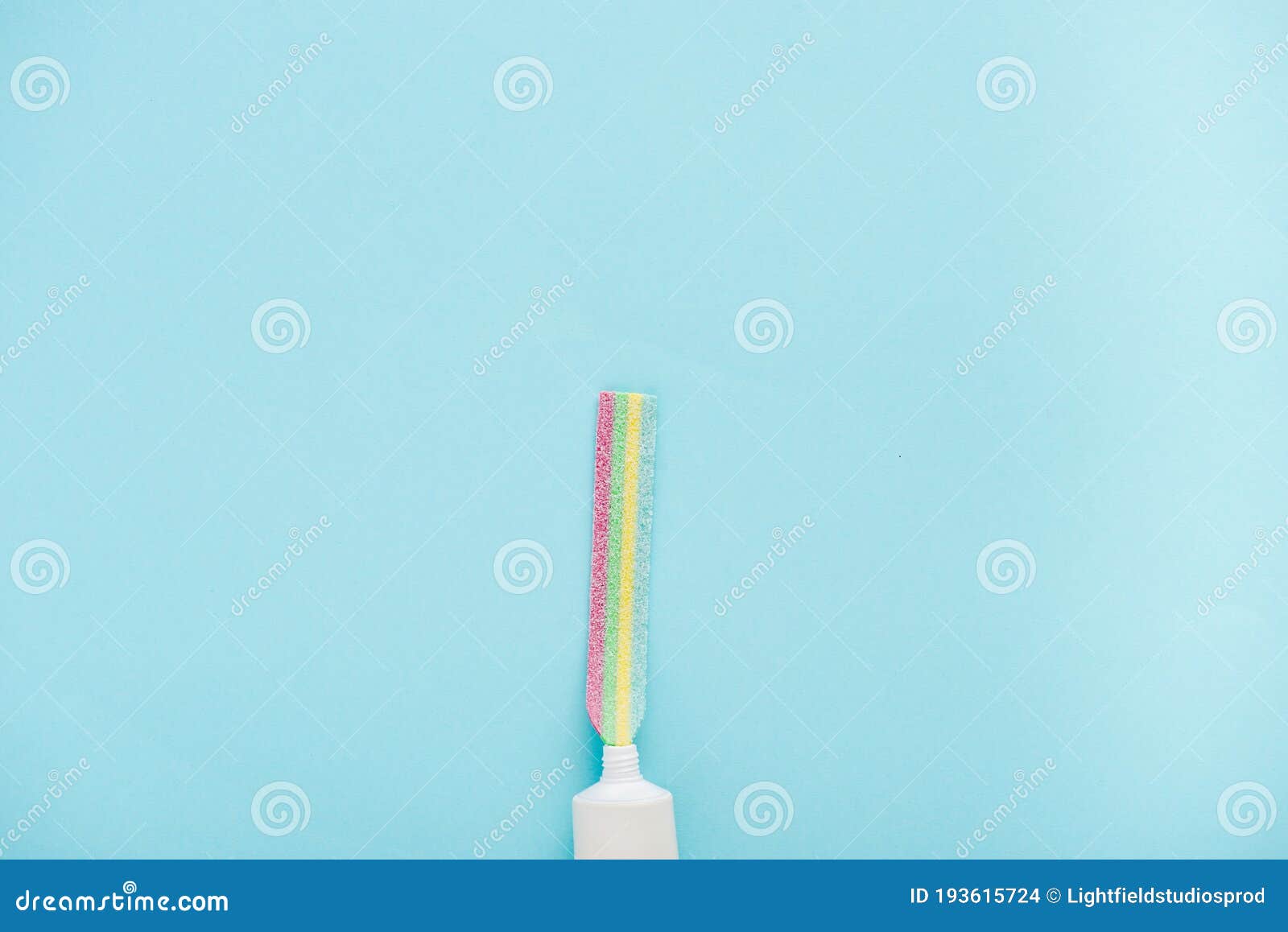 View of Toothpaste Tube with Chewing Colorful Candy Isolated on Blue