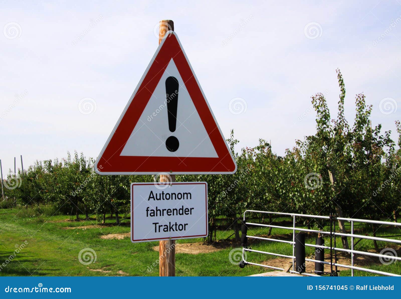 view on triangular warning sign on apple fruit tree plantation. german text means: autonomous driving tractor