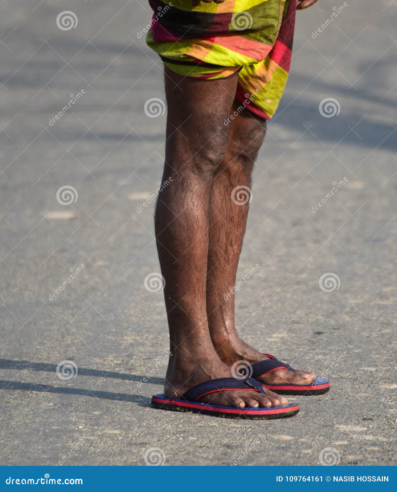 Man is standing on a street with wet legs stock photograph. A village worker is standing on a street with his wet legs and in slippers background photograph.