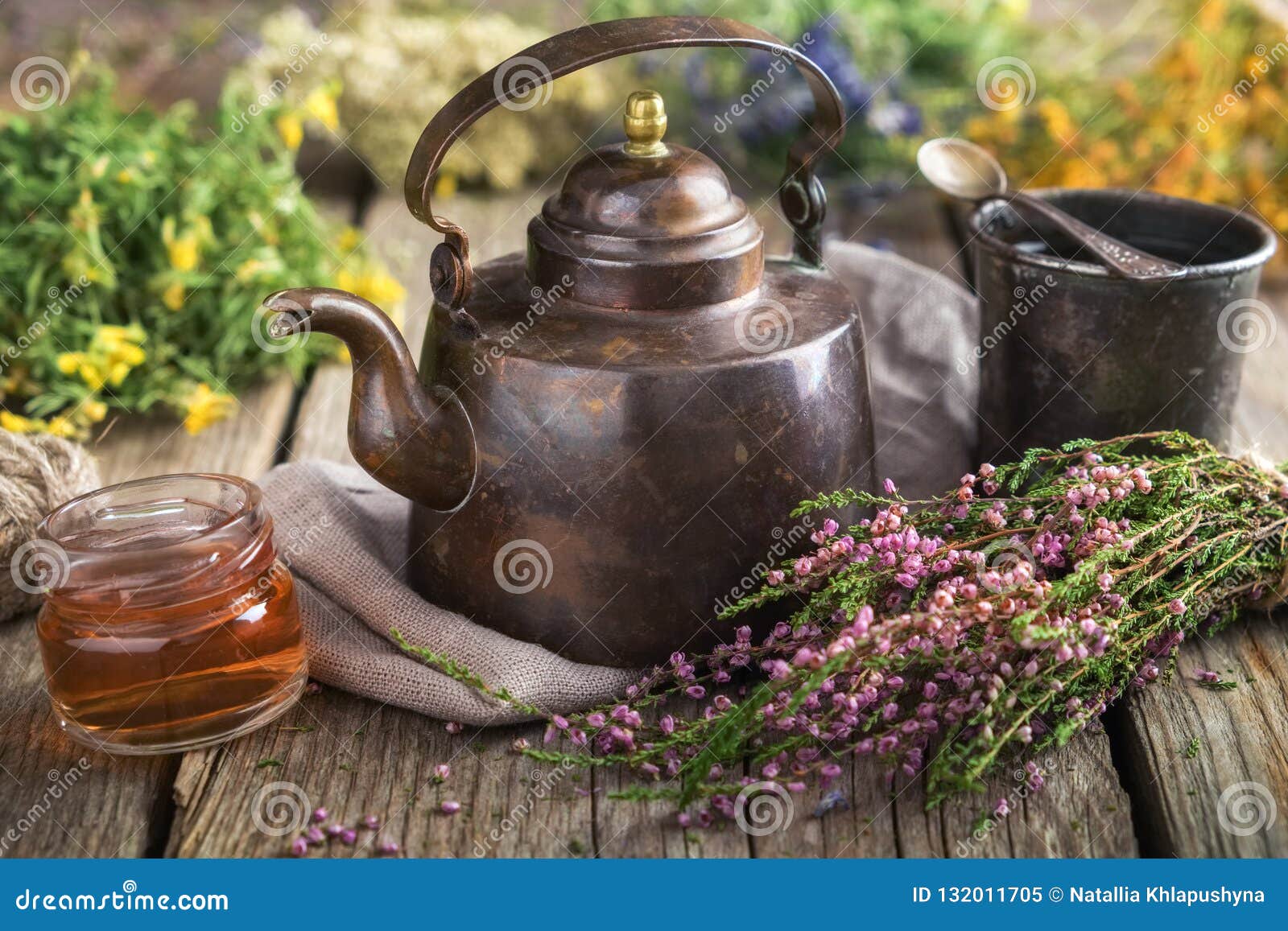 vintage teapot, cup of herbal tea, honey jar, medicinal herbs bunches on background.