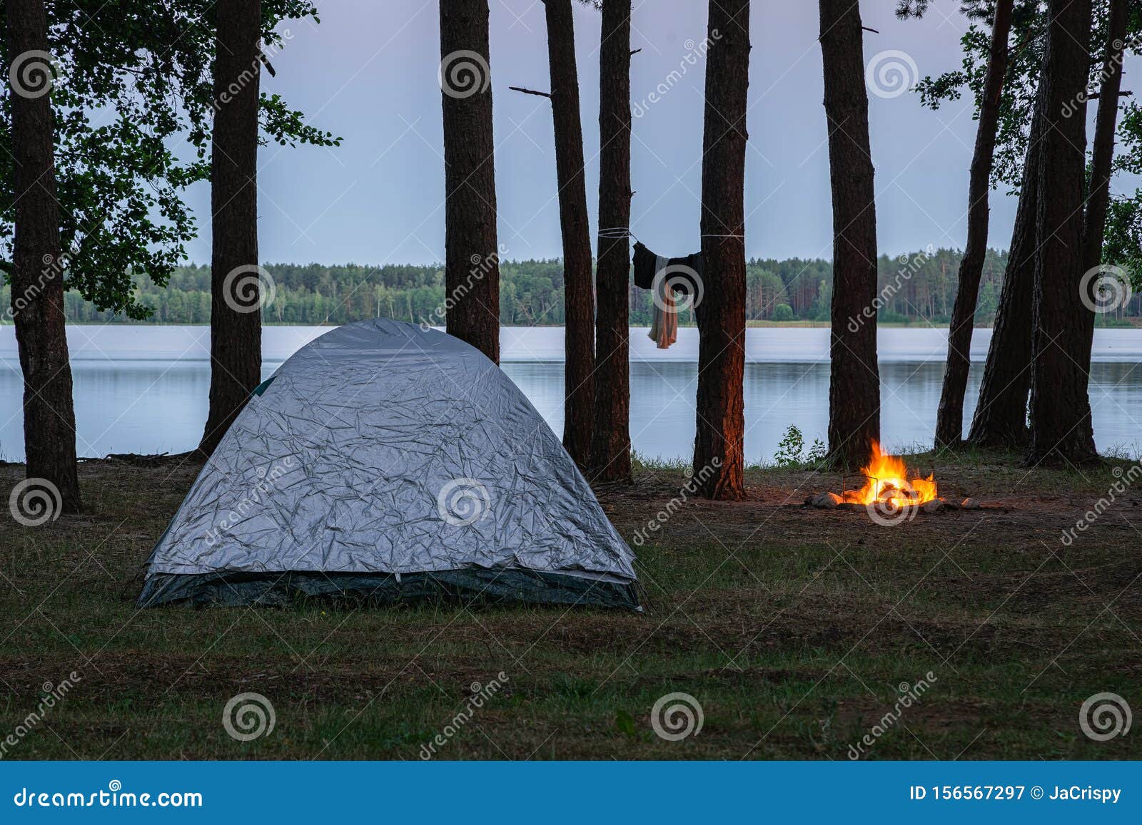 Vista Del Camping Junto Al Lago a La Luz Del Sol. Tienda Y Fuego Ardiente  Junto Al Agua Rodeada De Ã¡rboles En El Bosque. Gasto Imagen de archivo -  Imagen de chimenea