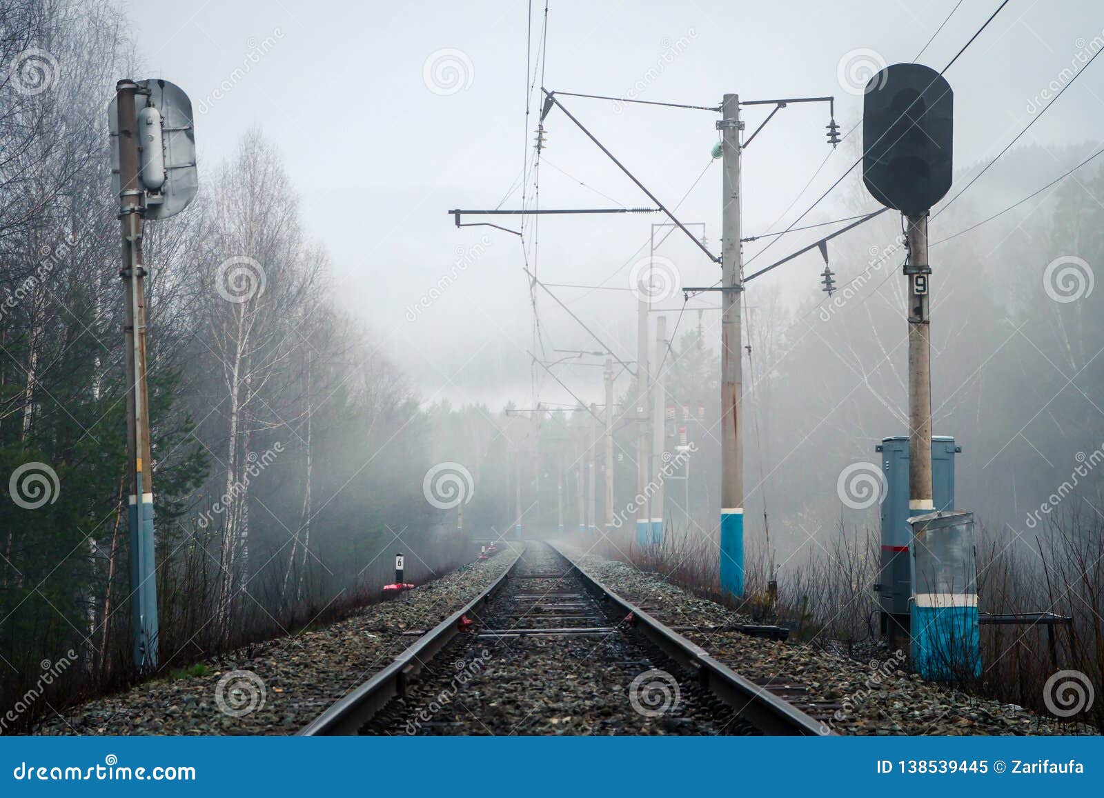 Vista del ferrocarril, de los semáforos y de los polos eléctricos en niebla en primavera. Vista del ferrocarril, de los semáforos y de los polos eléctricos en niebla por la tarde de la primavera