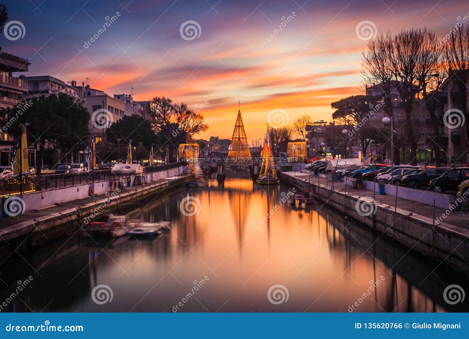 Vista scenica dell'albero di Natale su un ponte al tramonto, con le nuvole arancio Immagine lunga di esposizione in Riccione, Emilia Romagna, Italia