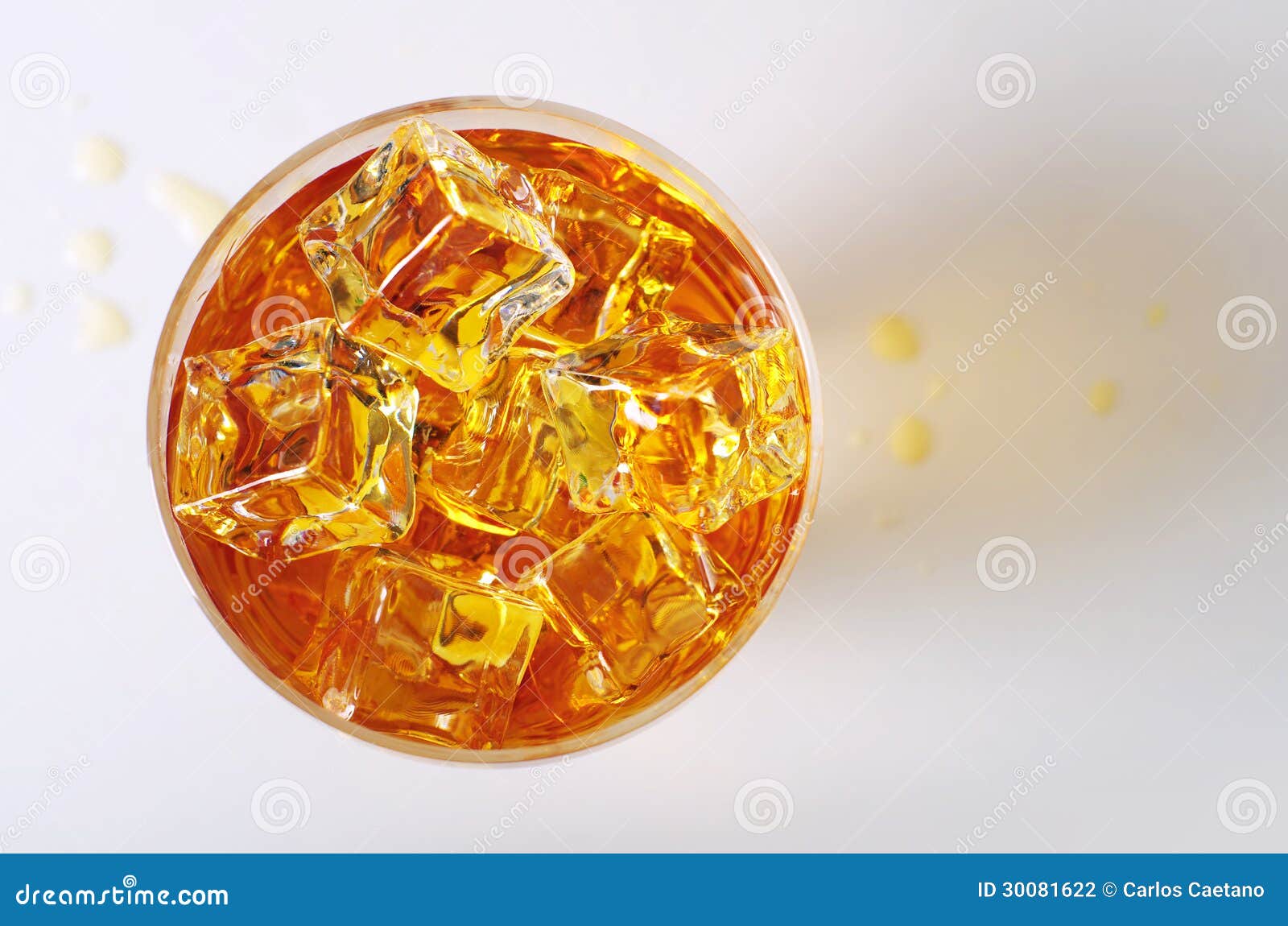 Vista superiore sulla bevanda alcolica in un vetro con i cubetti di ghiaccio e gocce rovesciate sulla tavola