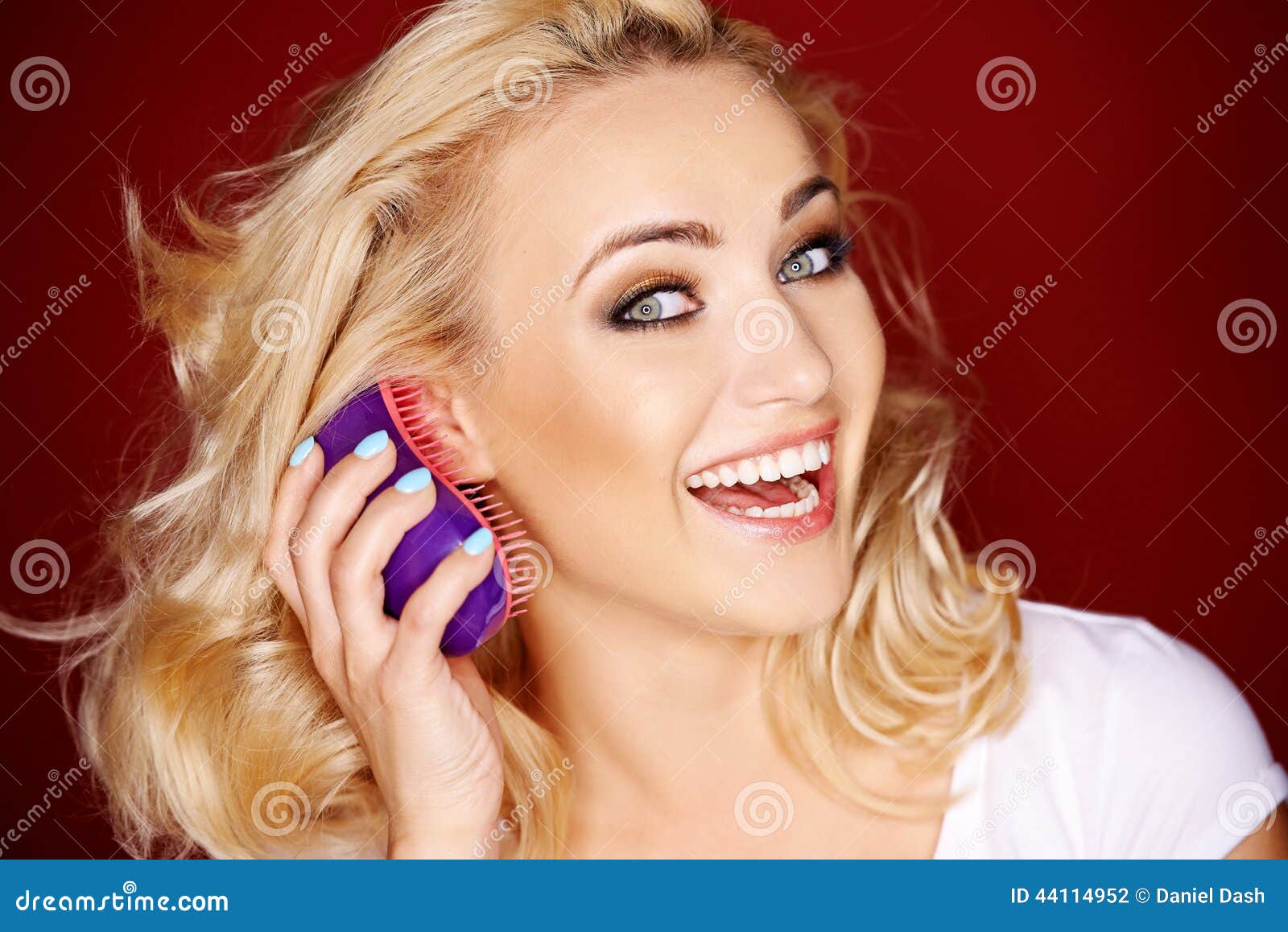 Vivacious blond woman brushing her hair as she looks sideways at the camera with a playful laugh.