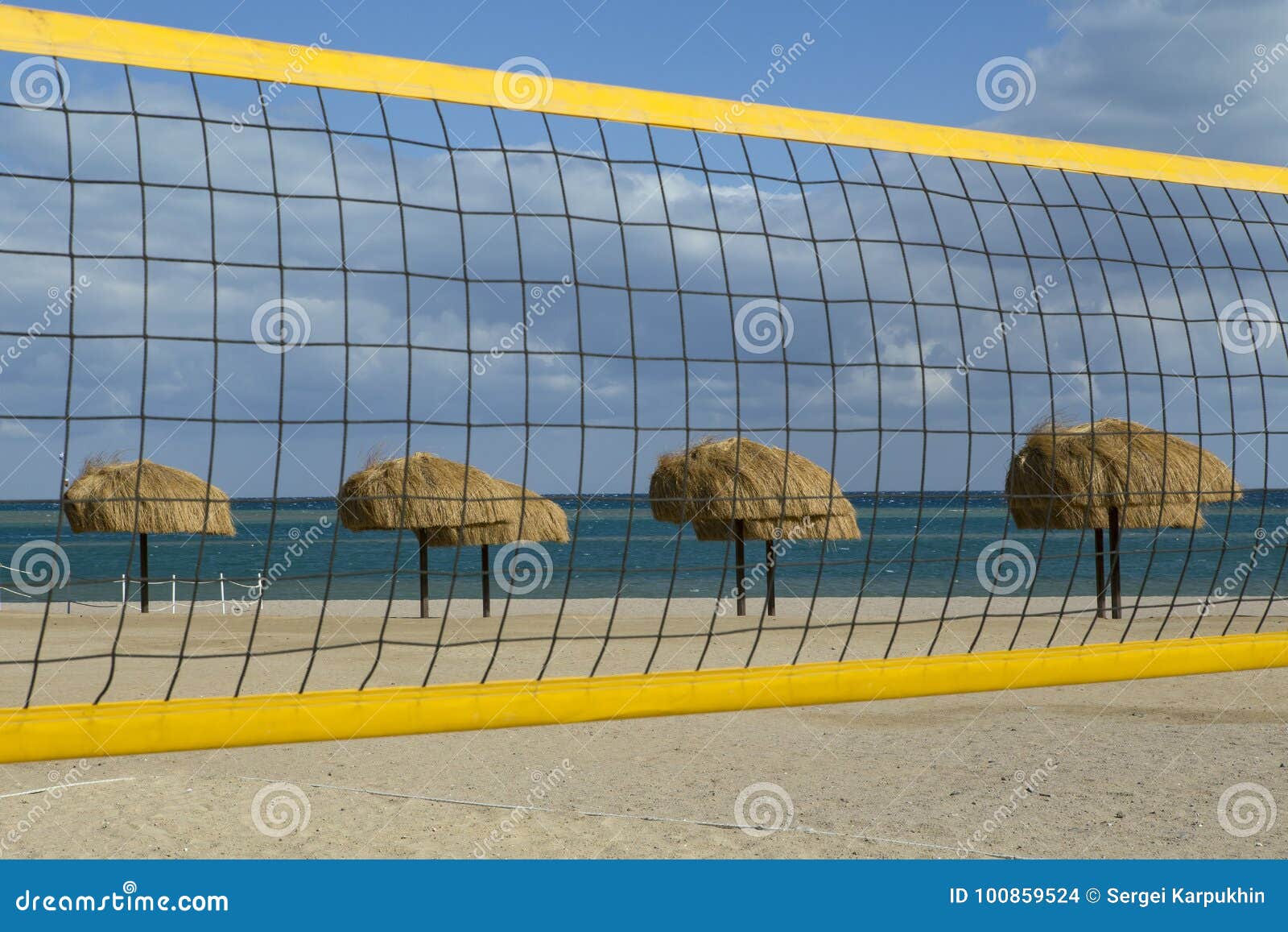 A Volleyball Net and Thatched Umbrellas on the Beach. Stock Photo