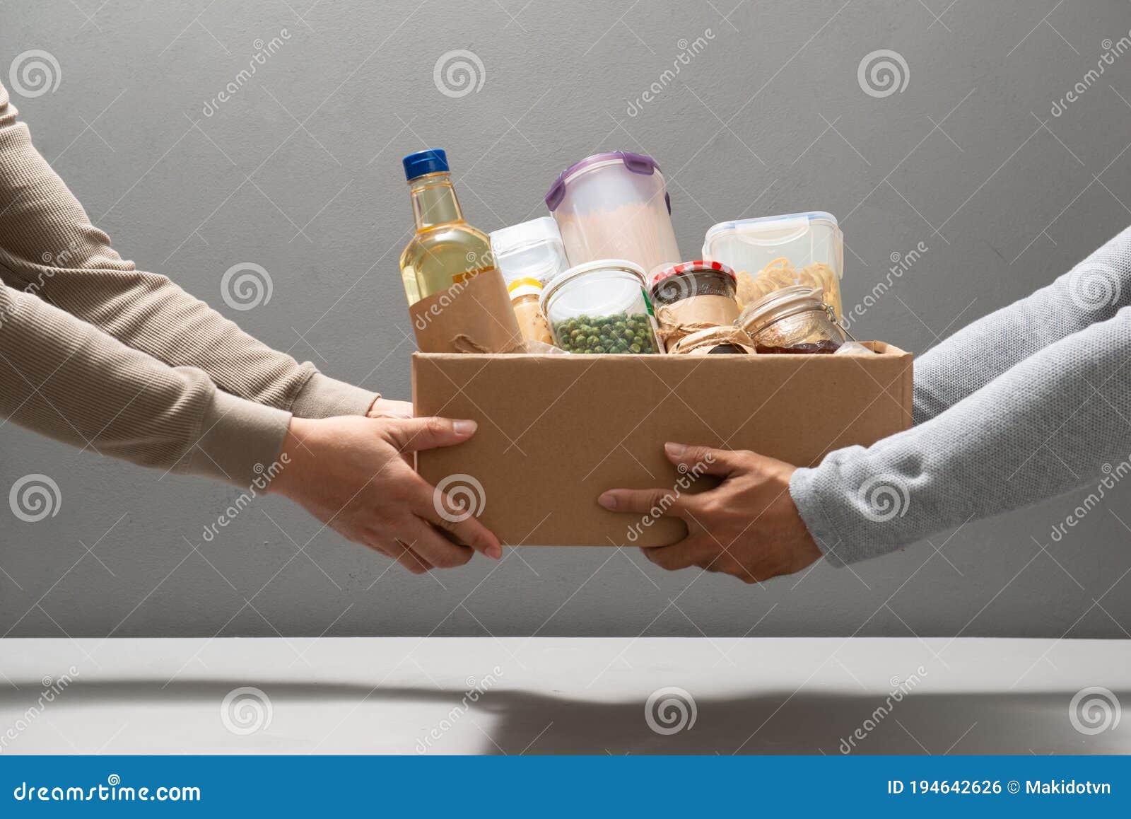 volunteers with donation box with foodstuffs on grey background