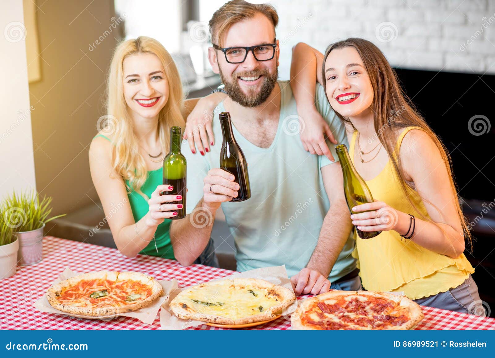 Vrienden die pizzapartij hebben thuis. Het portret van de jonge vrienden kleedde zich terloops in kleurrijke t-shirts die lunch met pizza en bier hebben thuis