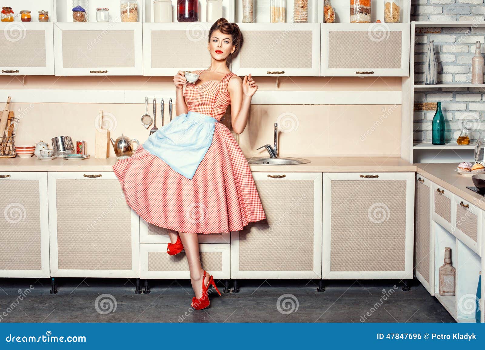 Vrouw in de keuken. Vrouw in een schort in keuken het drinken van een kop en het golven