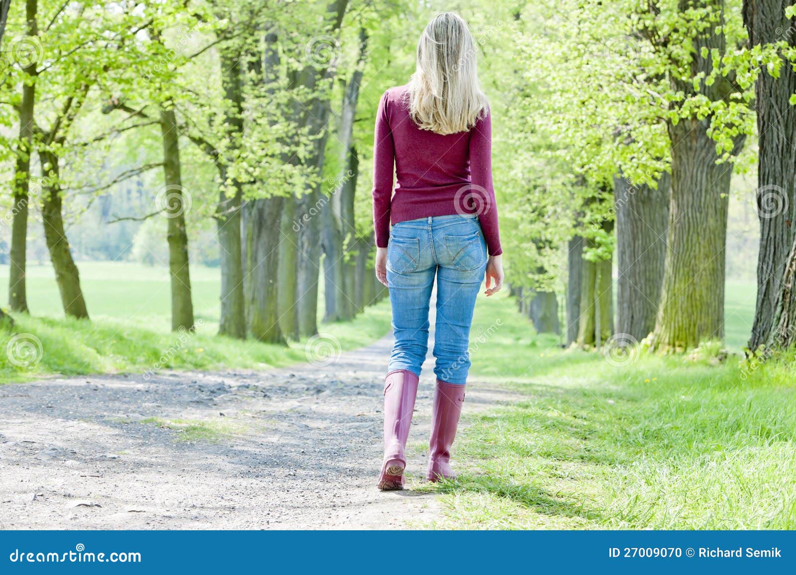 Vrouw in de lentesteeg. Vrouw die rubberlaarzen draagt die in de lentesteeg lopen