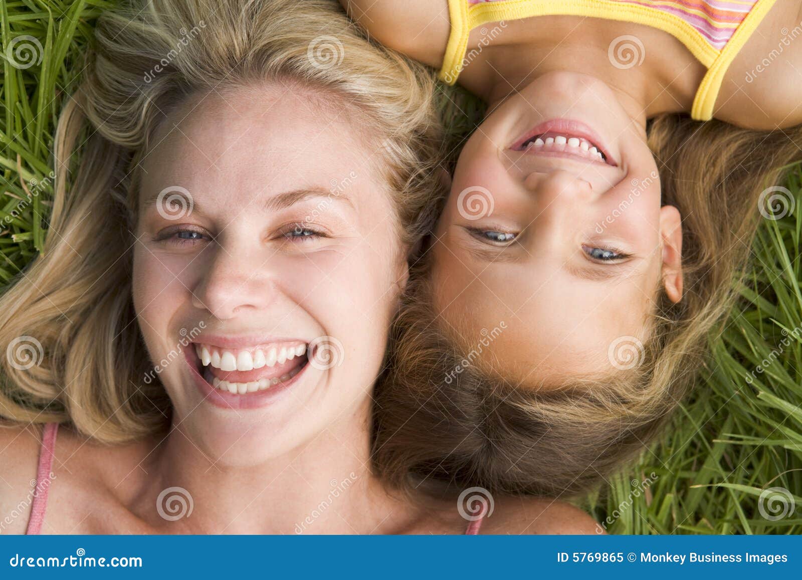 Vrouw en jong meisje die in gras het lachen liggen. Sluit omhoog van Vrouw en jong meisje liggend in gras het lachen