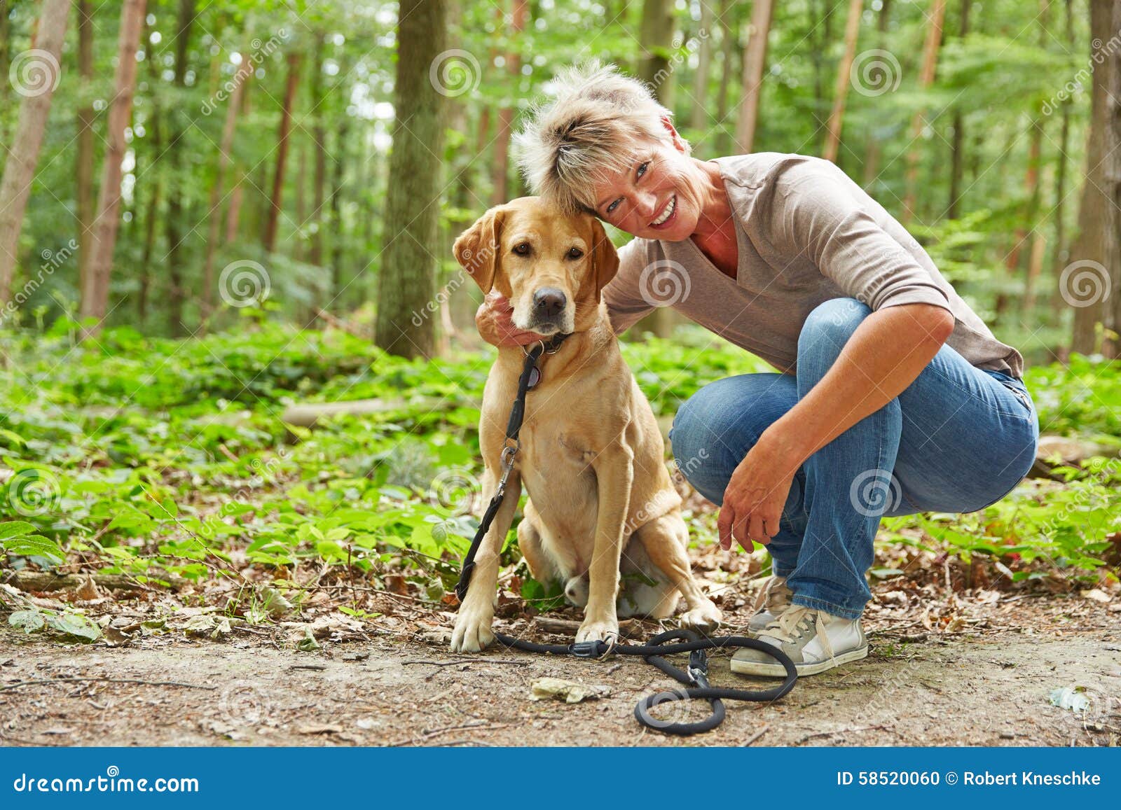 Vrouw met labrador retriever in bos. Gelukkige bejaardezitting met labrador retriever in een bos