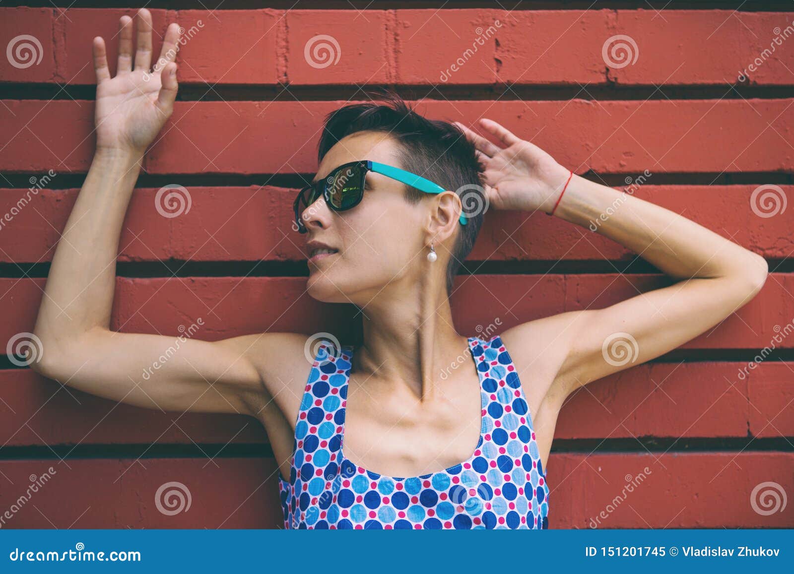 Vrouw tegen de achtergrond van een rode bakstenen muur Het brunette met glazen loopt onderaan de straat Meisje het stellen dichtbij de muur