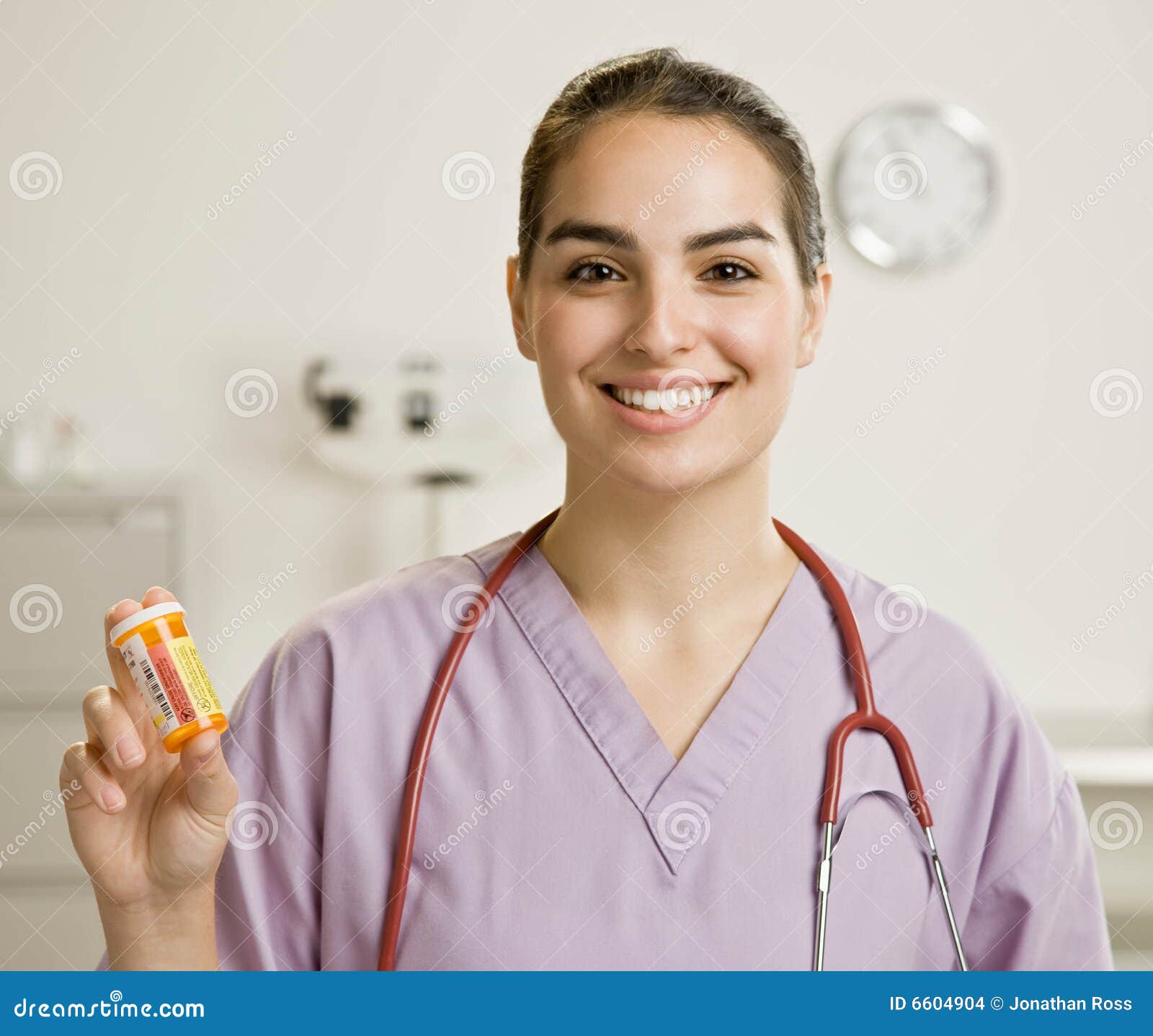 Vrouwelijke verpleegster het standhouden fles van medicijn. Het dragen van de verpleegster schrobben en de fles van het het voorschriftmedicijn van de stethoscoopholding