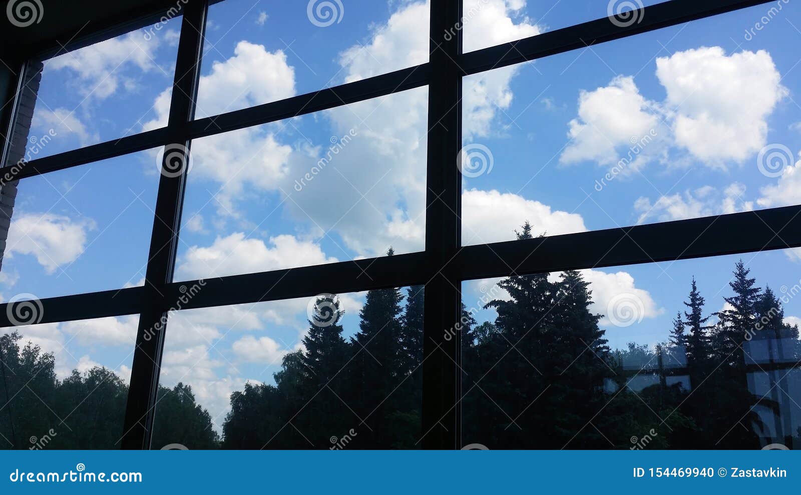 Vue de l'intérieur d'un immeuble de bureaux à travers une grande fenêtre sur le ciel avec des nuages et sur une forêt. Vue de l'intérieur d'un immeuble de bureaux à travers une grande fenêtre au ciel avec des cumulus sur fond et dans une forêt de conifères