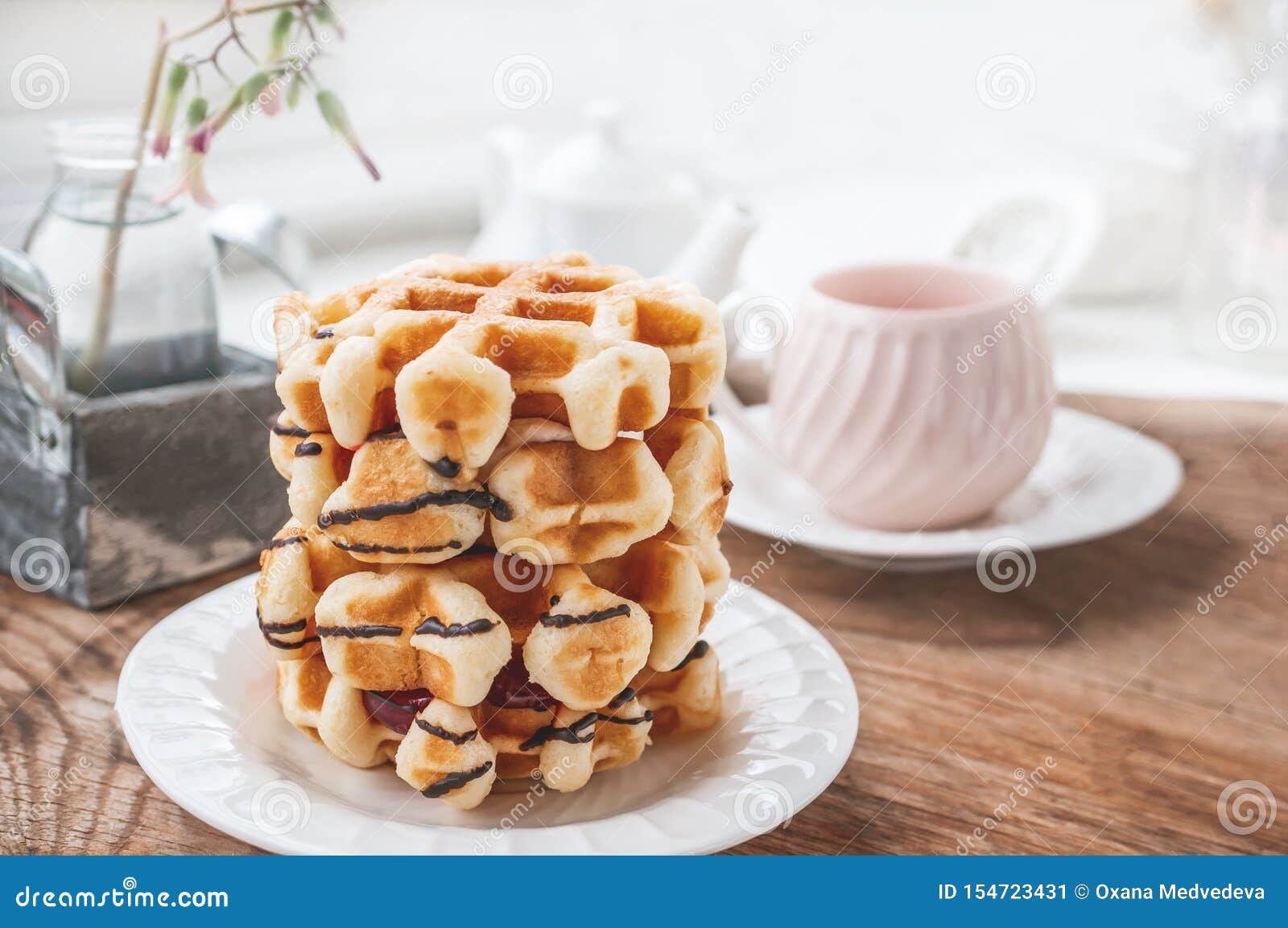 Waffles belgas do círculo fresco com uma camada de doce derramada com chocolate em uma placa branca com um copo do chá Fim acima