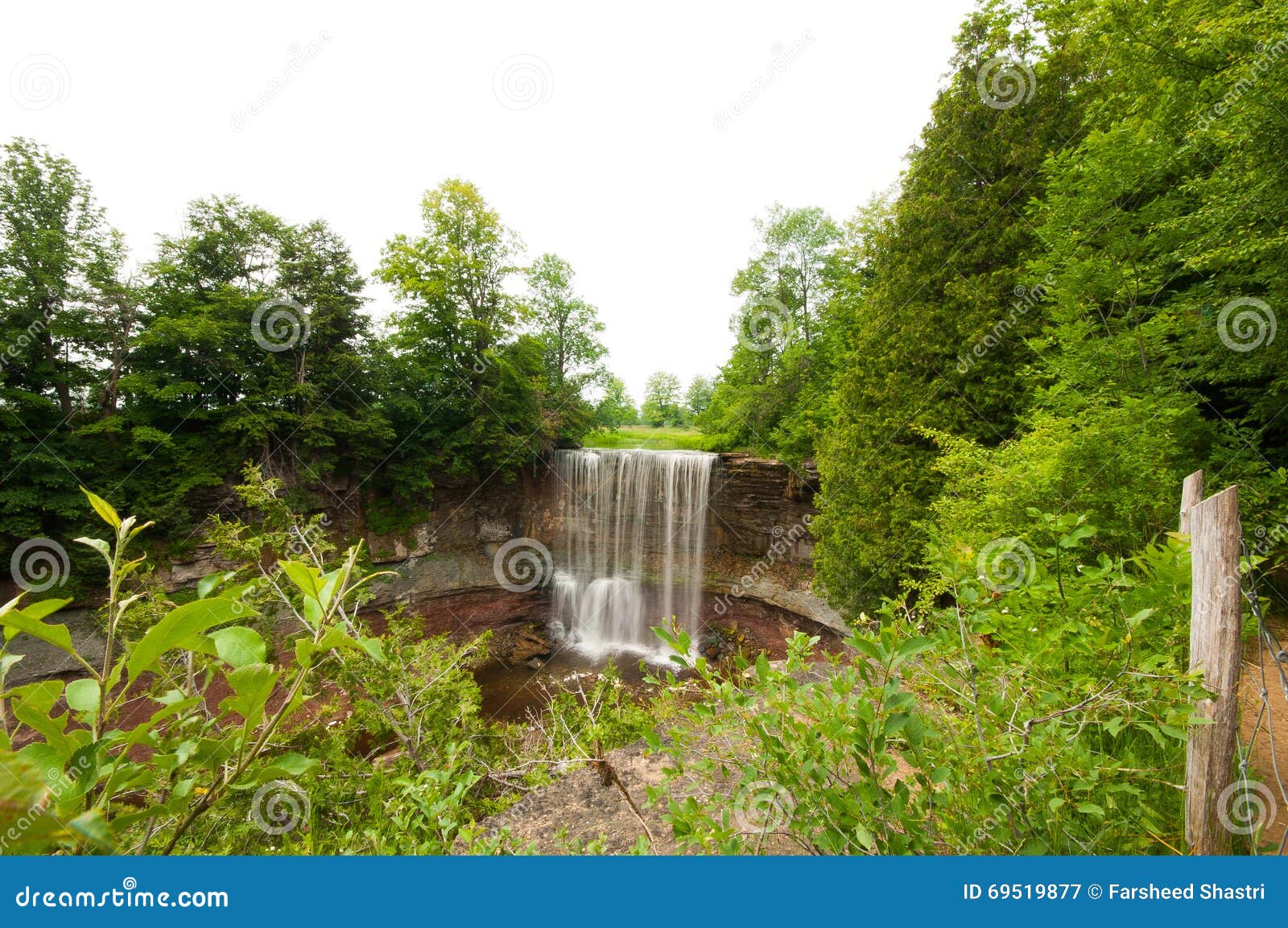 Waterval van rotsachtige klip in bos met groene bomen en duidelijke hemel