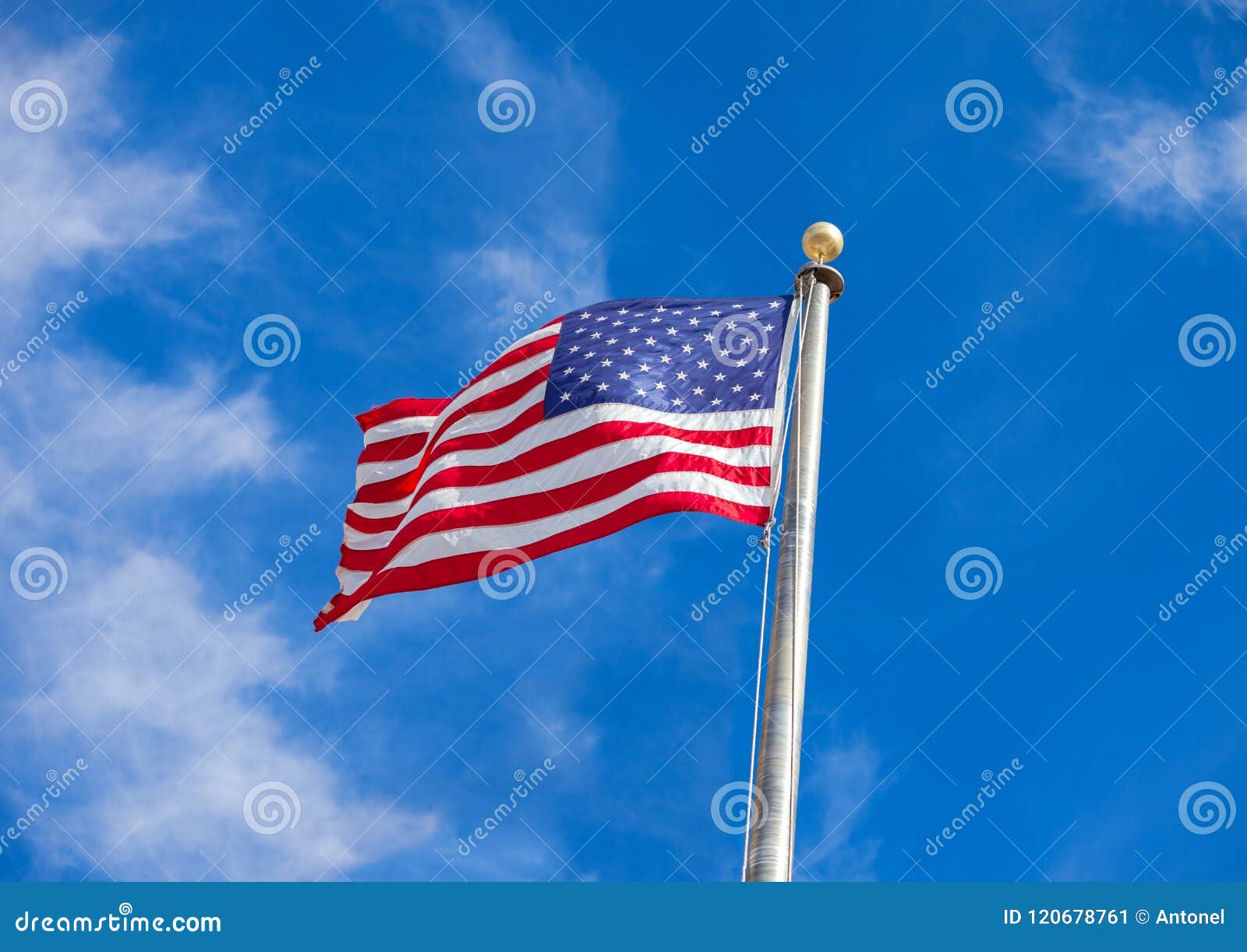 Waving Flag Of The United States Against The Blue Sky With White Clouds
