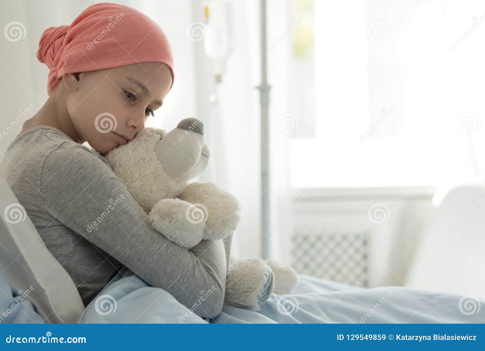 weak girl with cancer wearing pink headscarf and hugging teddy bear