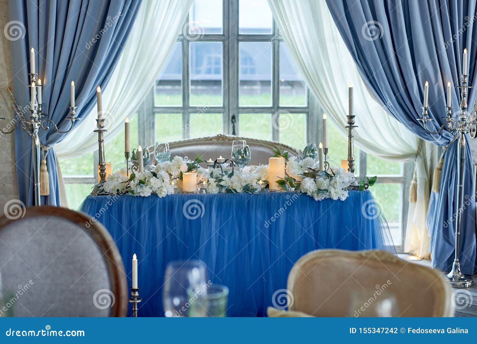 wedding table decorated with white flowers, candles. soft sofa with cushions, large window.blue and white.