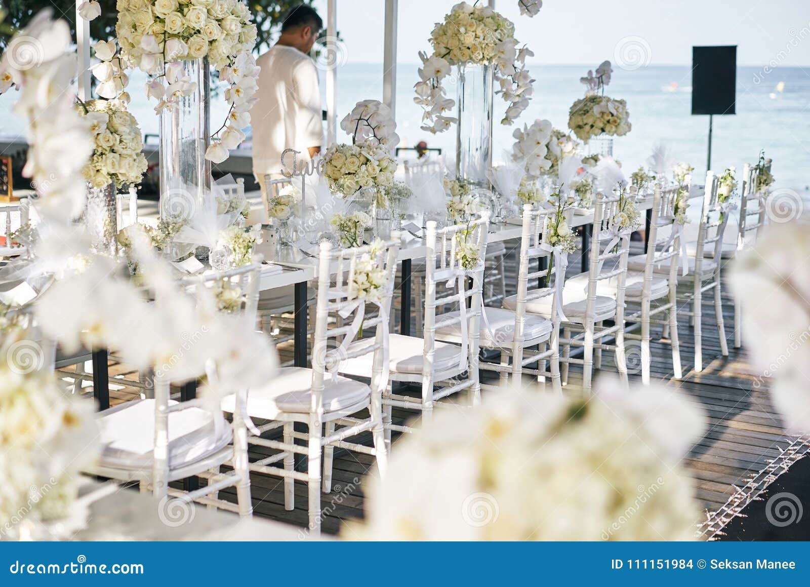 the wedding venue for reception dinner table decorated with white orchids, white roses, flowers, floral, white chiavari chairs