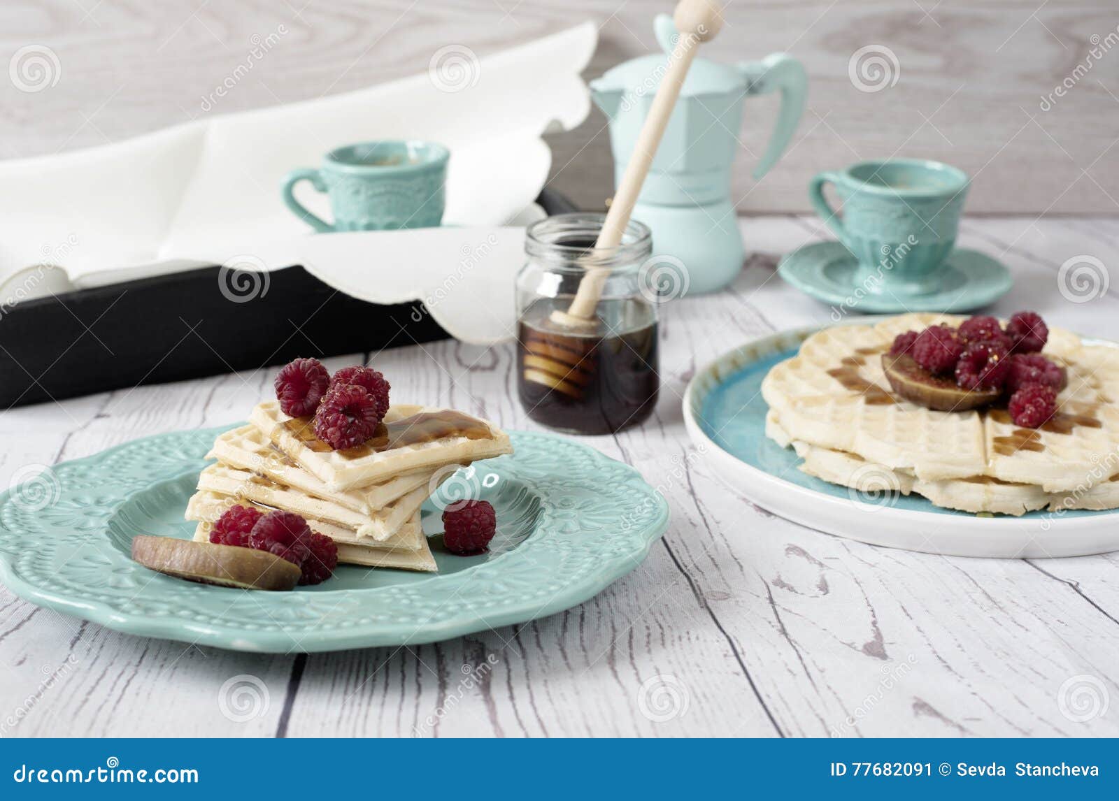 Weiches belgisches Herz formte Waffeln mit den Himbeeren und Feigen, bedeckt mit Honig auf Türkisblauplatte Ein Behälter des Kaffees und der Kaffeemaschine Rustikaler hölzerner Hintergrund, Draufsicht Feiertagsmorgen zu Hause