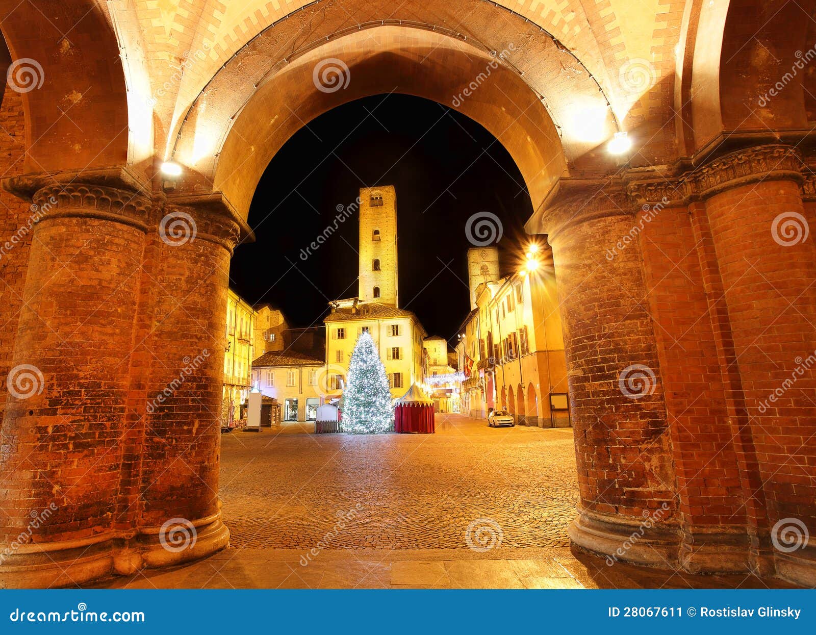 Weihnachtsbaum auf Stadtplatz. Alba, Italien. Weihnachten belichtete Baum auf Stadtplatz vor alten Kontrolltürmen in der historischen Mitte als gesehener durch Ziegelsteinbogen in, Norditalien alba.