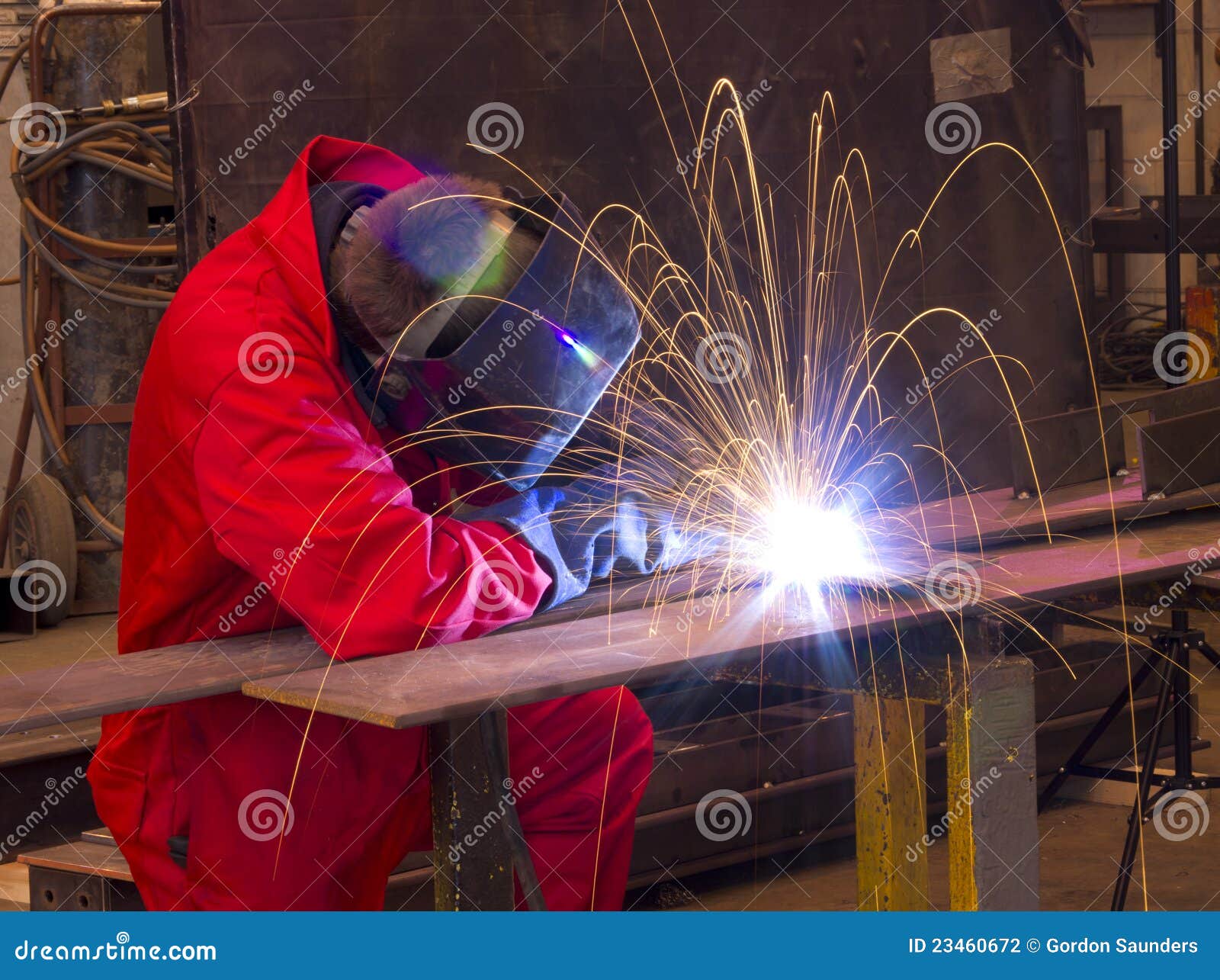 welder bends to cut metal beam with orange sparks.