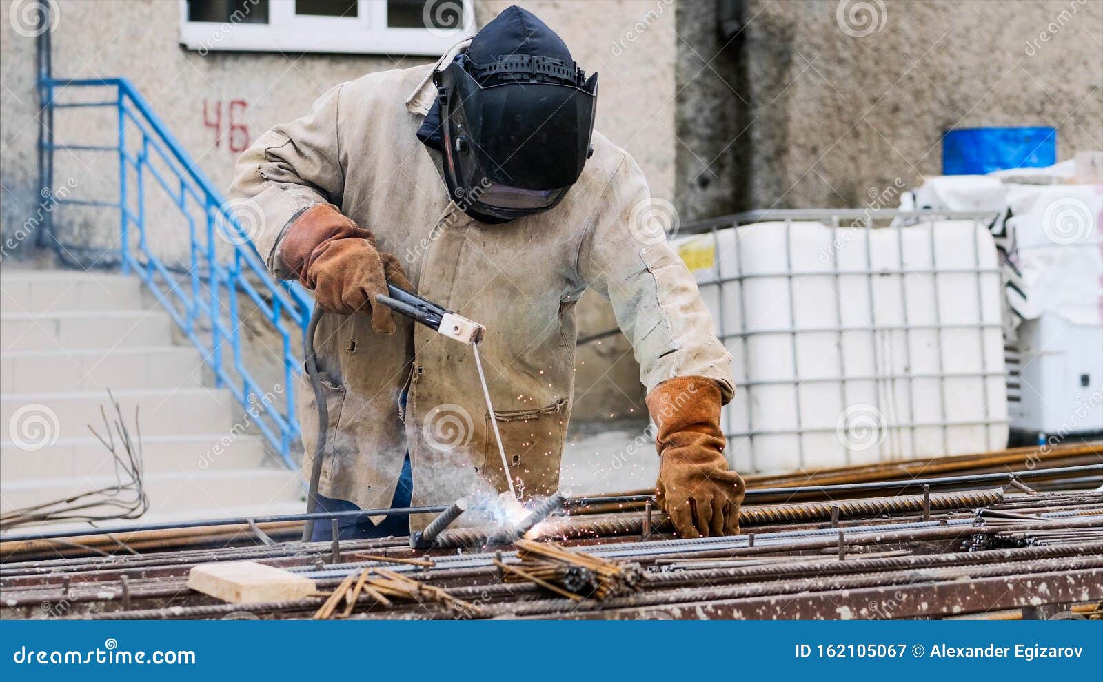 Welder at Construction Site is Welding Pipe with Electrode in Helmet