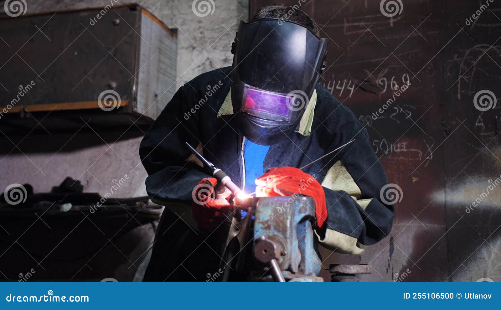 A Welder in a Welding Mask and Work Gloves Welds a Part Clamped in a