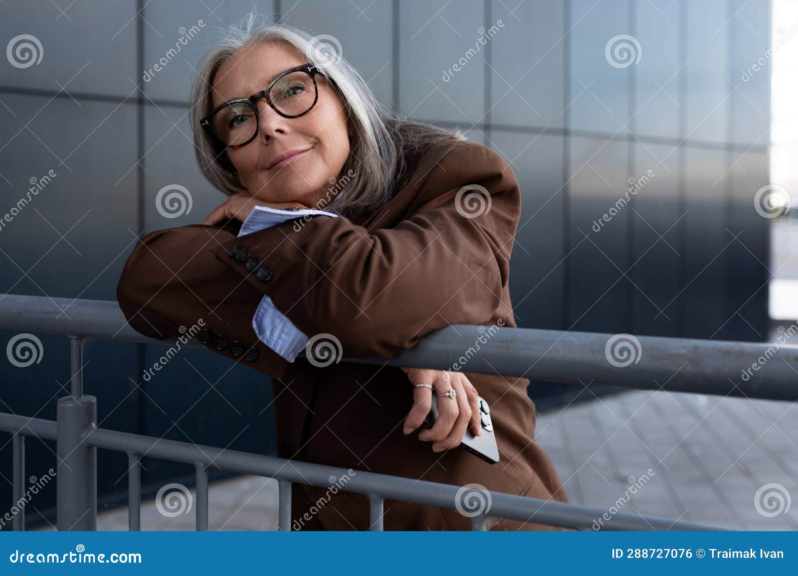 Well Groomed Elderly Gray Haired Business Woman In A Brown Jacket And Trousers Walks In An Urban