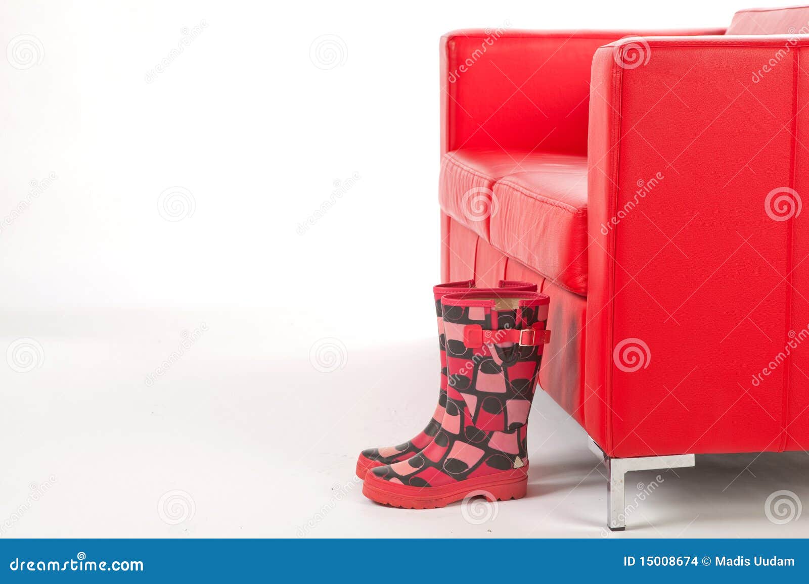 Wellingtons na frente de um sofá vermelho. Pares de Wellingtons à moda na frente de um sofá vermelho em um fundo isolado branco