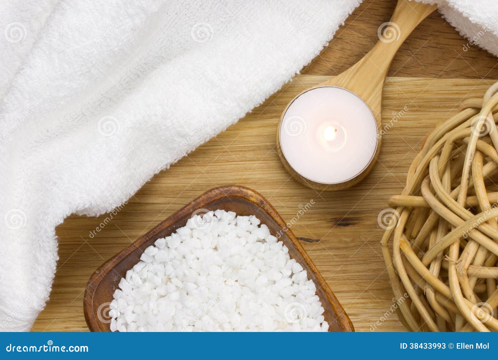 wellness candle on a wooden spoon with towel and bath salt