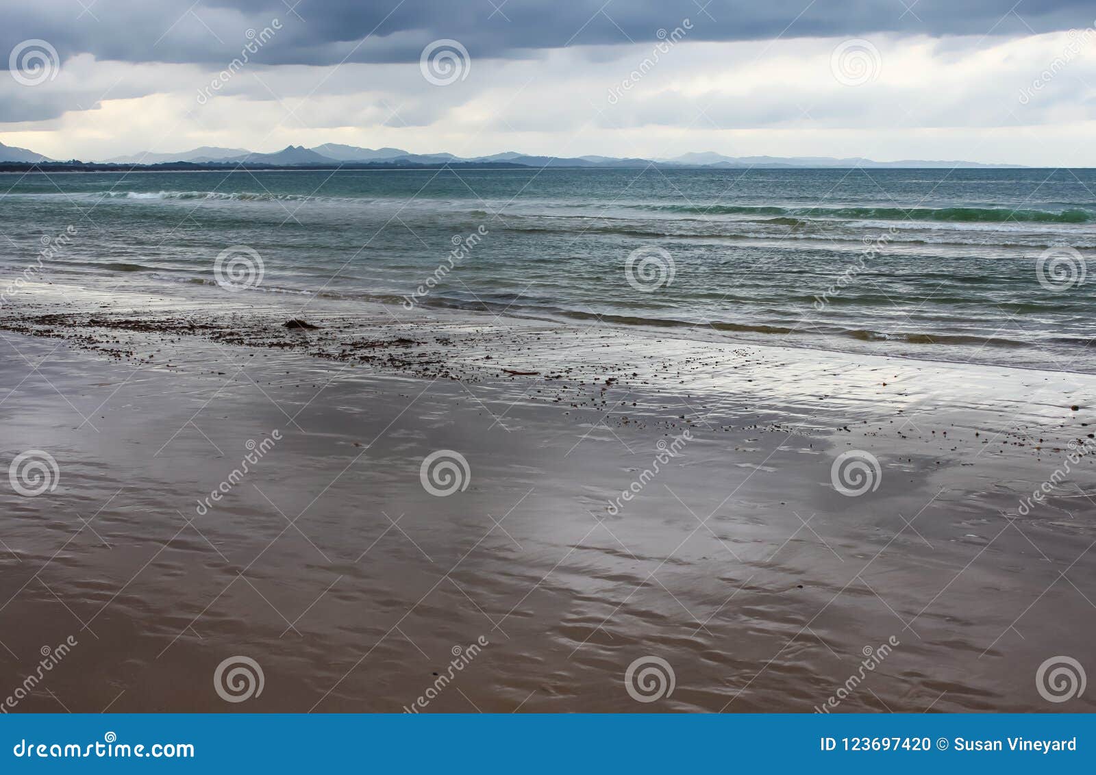 wet beach as the tide recedes with blue mountains ranges in the distance under a stormy sky - byron bay nsw australia
