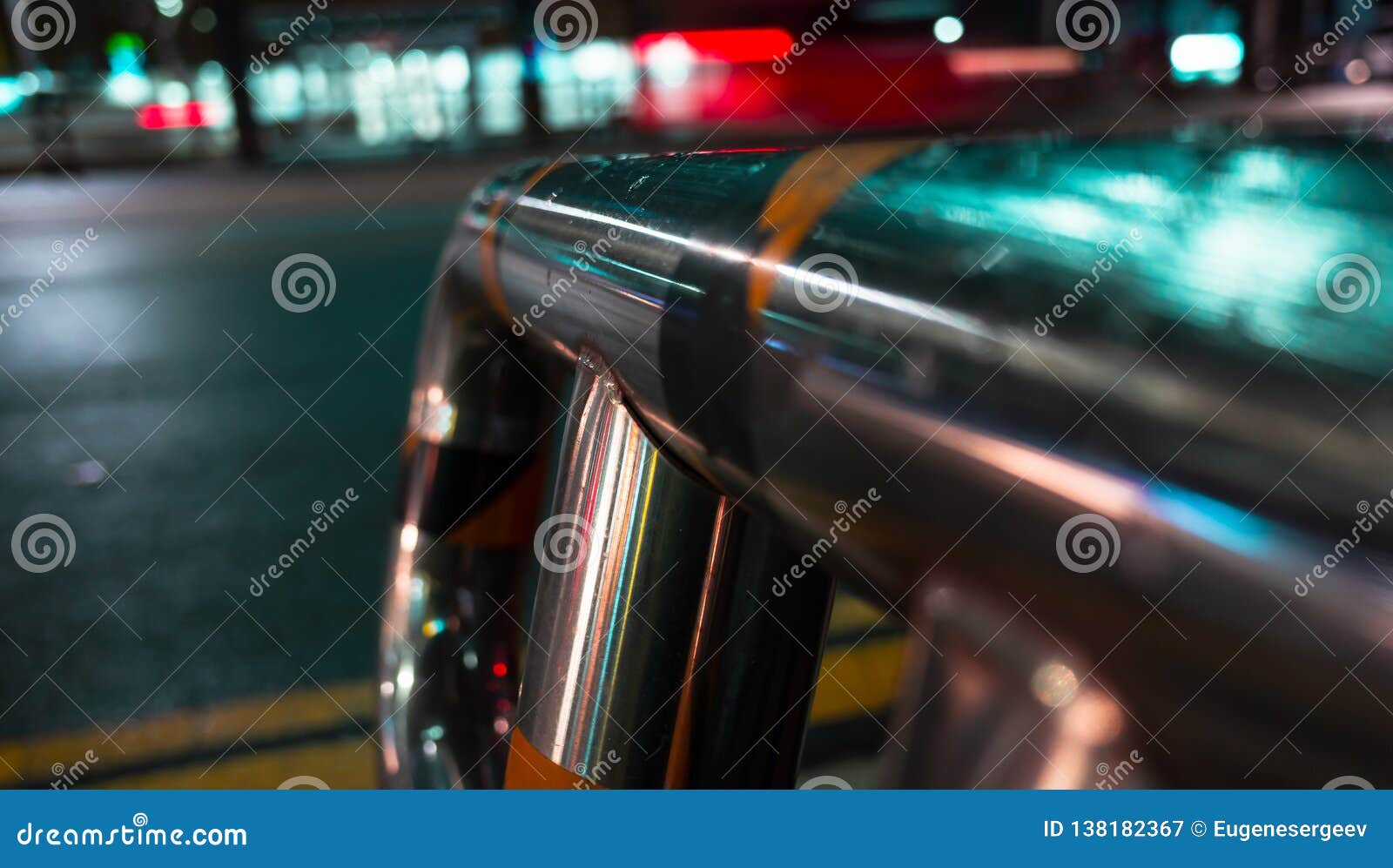 Abstract night city background with wet steel railing near urban road